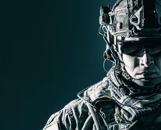 Elite member of US Army rangers in combat helmet and dark glasses. Studio shot, dark black background, looking at camera, dark contrast